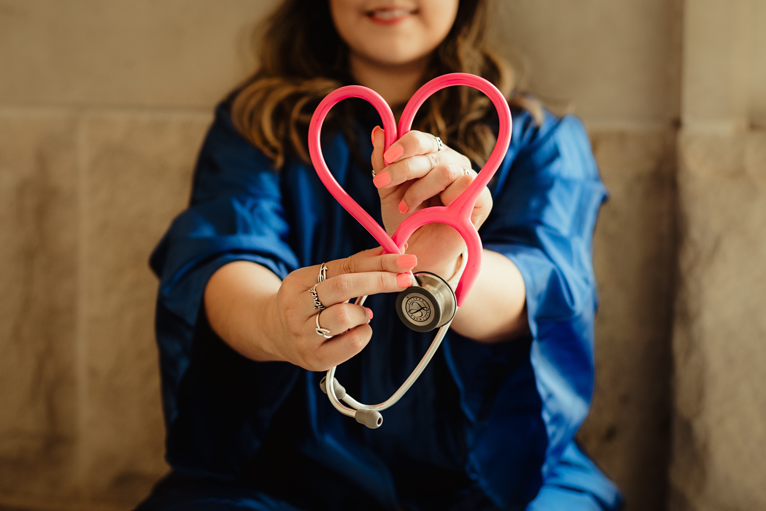 Person in Krankenpflegerinnenkleidung hält ein Stethoskop, das in Herzform gebogen ist