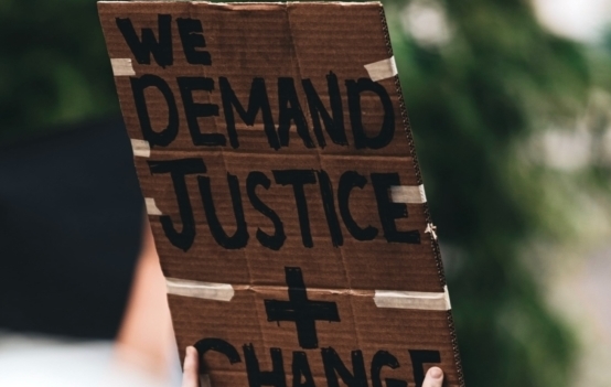 Foto einer Hand, die ein Plakat hält mit der Aufschrift "We demand justice and change"