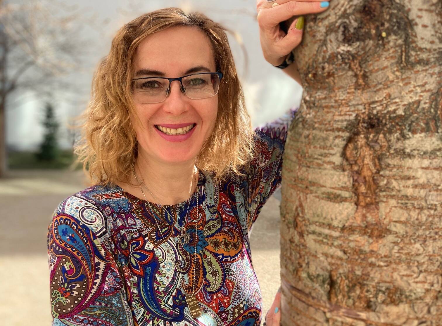 Victoria Aharonov hat lange dunkelblonde Haare, trägt eine Brille und eine gemusterte Bluse